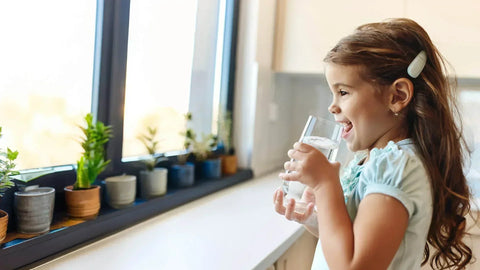 Young girl drinking filtered water in a glass at the kitchen bench.