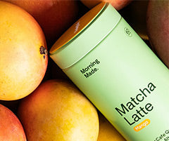 Morning Made Matcha Latte Mango - green canister laid down amongst a bunch of whole mangos.