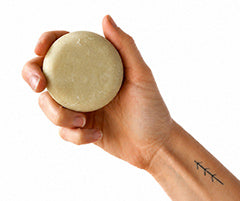 Hand holding bar of solid shampoo, on a white background.