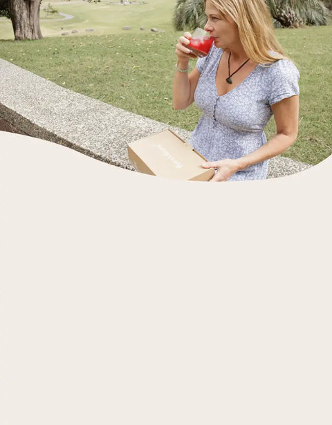 Woman sitting outdoors, drinking from a glass and holding a book