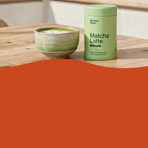 A light green cylindrical canister labeled 'Morning Nook Matcha Latte' stands on a wooden table next to a matching glazed ceramic cup containing a green matcha latte. A large solid orange shape overlays the lower half of the image.