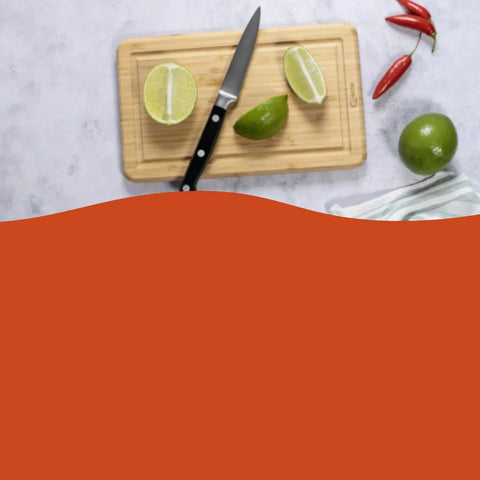 A kitchen scene with a wooden cutting board, a black-handled knife, lime halves and a whole lime, plus red chili peppers on a light marble surface. A large solid orange shape overlays the lower half of the frame.