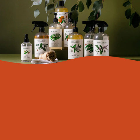 A group of Nuna Eco natural cleaning products, including spray bottles and a pump dispenser, arranged on a green surface with a large orange graphic overlay covering the bottom half of the frame.