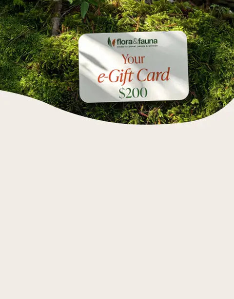 A white rectangular e-Gift Card for flor&fauna with a $200 denomination, placed on a bed of green moss outdoors. The card features the flor&fauna logo and text in green and red.