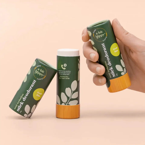 Two tubes of natural stick deodorant displayed on a warm peach background. One tube is held by a hand, one is standing upright.