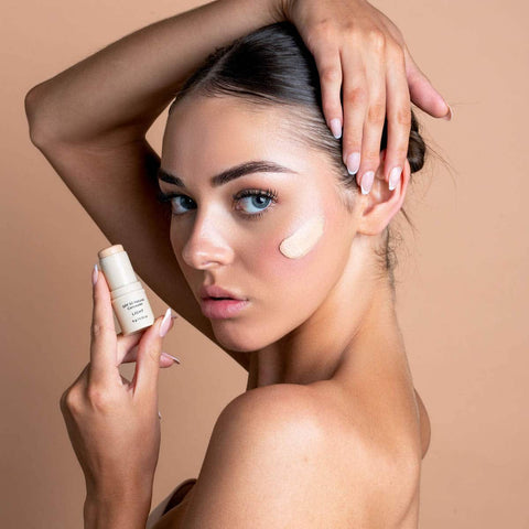 Woman modelling a concealer swatch on her cheek while holding the light concealer. 