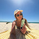 Woman on a beach holding a tube of sunscreen.