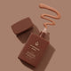 Avocado Zinc bronzer + sunscreen bottle with lid off showing a swatch of product on a brown background