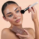 Woman applying makeup with a brush and product container against a beige background