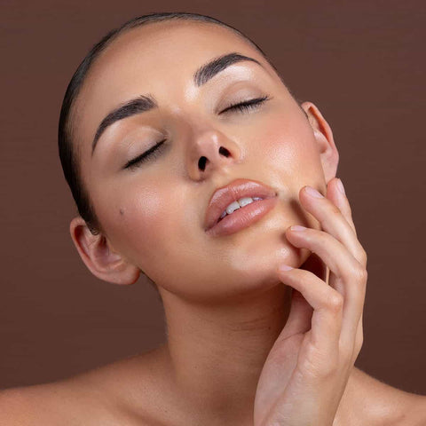 Woman with a close-up of her face after applying glow drops against a brown background