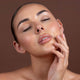 Woman with a close-up of her face after applying glow drops against a brown background