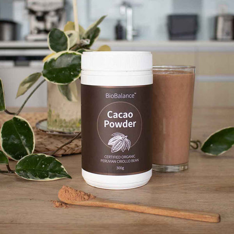 BioBalance Cacao Powder container with a glass of cacao drink and spoon on a wooden surface.