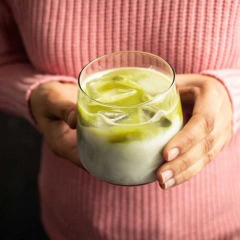 Person holding a glass of iced matcha latte with a pink sweater.