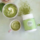 Two cups of matcha green tea with a container of BioBalance Matcha Powder on a light background.