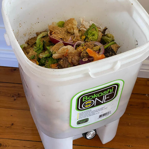 White Bokashi One filled with food waste on a wooden floor.