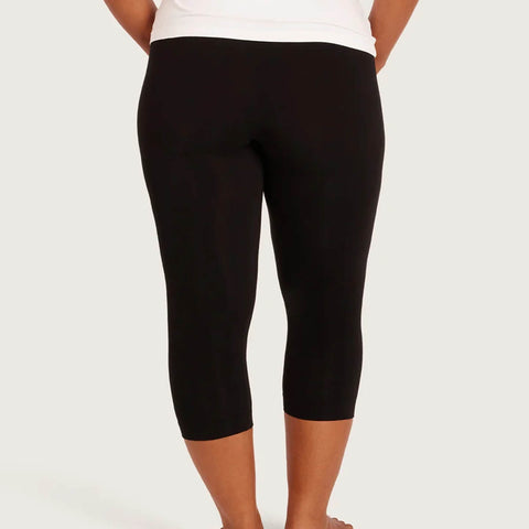 Black capri leggings shown from the back on a model, paired with a white top, against a light gray studio background.