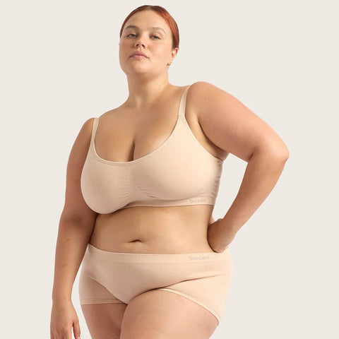 A plus-size model wearing a matching beige/nude bra and underwear set against a solid light grey background.