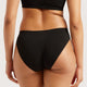 Rear view of a model wearing black high-waisted briefs with a side cutout, paired with a black sports bra against a light gray studio background.