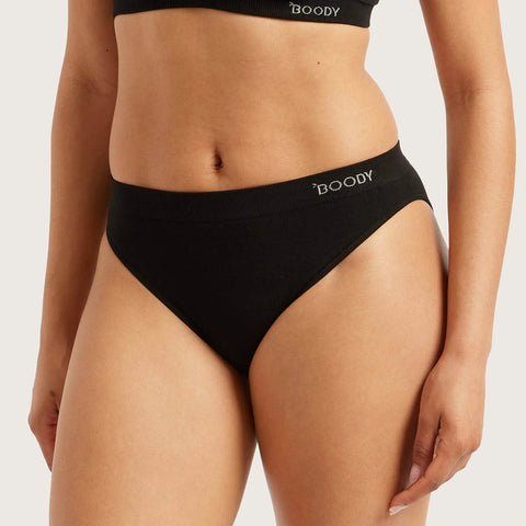 A close-up of a model wearing black high-waisted briefs with the brand name 'BOODY' printed in white on the waistband, against a light gray studio background.