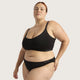 A plus-size model wearing a black two-piece lingerie set with a scoop-neck bralette and matching high-waisted briefs, featuring the 'boody' brand logo on the waistbands, set against a solid light gray background.