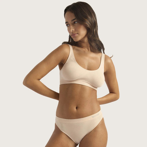 A woman modeling a light beige seamless bra and matching underwear set against a solid light gray background.