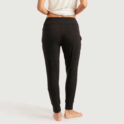 Rear view of a model wearing black high-waisted lounge pants with side pockets, paired with a white cropped top, against a pale studio background.