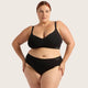 A plus-size model wearing a black two-piece lingerie set with a bra and high-waisted briefs, featuring the brand name 'boody' printed in white on the side bands, set against a solid light beige background.