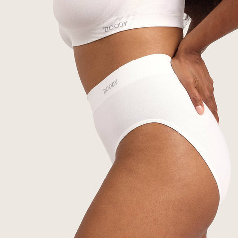 A close-up of a model wearing white high-waisted briefs and a matching white bra, with the brand name 'BOODY' printed on the waistband and underband.