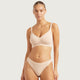 A model wearing a light beige two-piece lingerie set consisting of a bralette and matching high-waisted briefs, photographed against a solid light gray background.