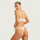 A model wearing a light beige two-piece lingerie set, featuring a bralette with adjustable shoulder straps and matching high-cut briefs, shown from a three-quarters back view against a solid light gray background.