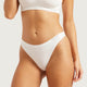A close-up of a model wearing white high-cut briefs with a visible 'Boody' brand logo on the waistband, paired with a matching white bra against a light gray studio background.