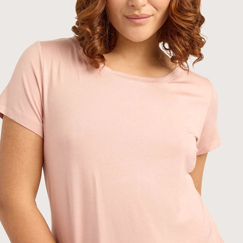 A woman with curly brown hair is shown from the back wearing a light pink short-sleeve top and matching pink bottoms against a light gray studio background.