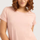 A woman with curly brown hair is shown from the back wearing a light pink short-sleeve top and matching pink bottoms against a light gray studio background.