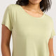 A woman wearing a pale sage green short-sleeve crewneck t-shirt, shown from the chest up against a light gray background.