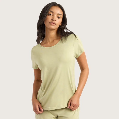 A woman modeling a light sage green short-sleeve crewneck t-shirt against a solid light gray background.