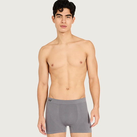 A shirtless man modeling gray boxer briefs against a light gray studio background.