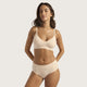 A woman modeling a matching beige bra and underwear set against a plain light gray studio background.