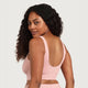 A woman with long, curly dark hair is shown from the back wearing a light pink ribbed sports bra and matching bottoms against a solid light gray background.