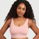 A woman with long, curly black hair wearing a light pink ribbed scoop-neck sports bra, shown from the chest up against a solid light gray background.