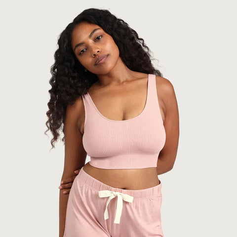 A woman modeling a light pink ribbed tank top and matching pink drawstring shorts against a light gray studio background.