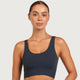 A woman wearing a dark navy ribbed scoop-neck sports bra against a light gray studio background.