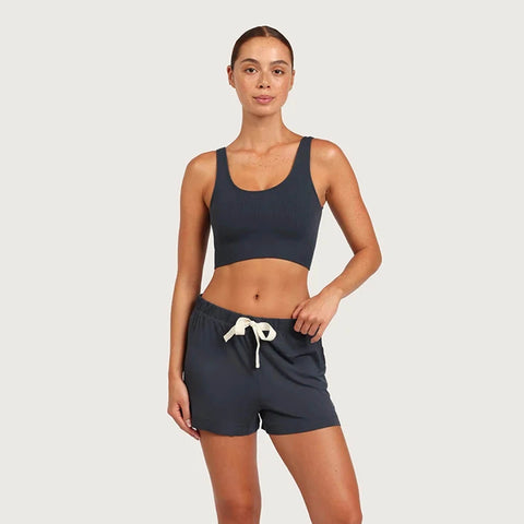 A woman modeling a matching two-piece activewear set consisting of a dark navy scoop-neck crop top and matching dark navy shorts with a white drawstring, set against a solid light gray background.