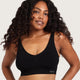 A woman with long, curly dark hair wearing a black scoop-neck sports bra with a small white 'boody' logo on the bottom right, set against a solid light beige background.