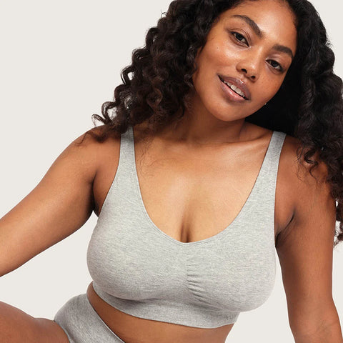 A woman wearing a light gray heather bralette and matching bottoms, photographed against a plain light gray studio background.