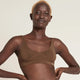 A model with short blonde hair wearing a brown ribbed scoop-neck bralette, posing against a solid light beige background.