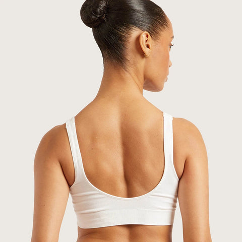 Rear view of a woman wearing a white ribbed sports bra against a light gray studio background.
