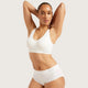 A woman modeling a white two-piece underwear set consisting of a scoop-neck bralette and matching high-waisted briefs, with the brand name 'boody' printed on the waistbands, against a solid light gray background.