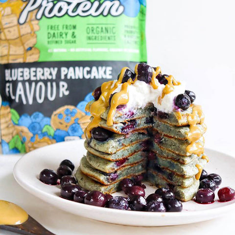 Blueberry pancakes on a plate with a packet of protein powder in the background.