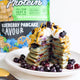 Blueberry pancakes on a plate with a packet of protein powder in the background.