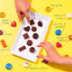 Assorted chocolate candies on a white tray with labelled flavours on a yellow background.